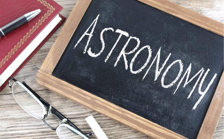 Image of a chalk board with astronomy written on it, there are glasses and a notebook and pen