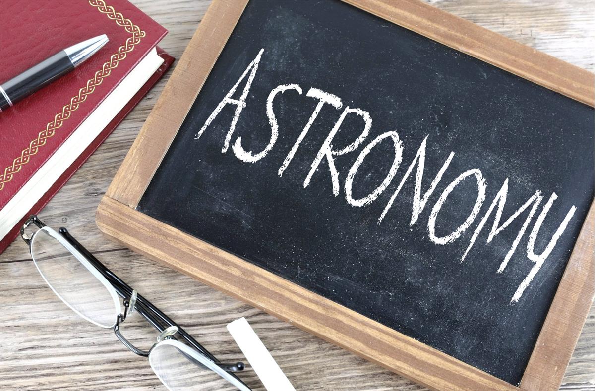 Image of a chalk board with astronomy written on it, there are glasses and a notebook and pen